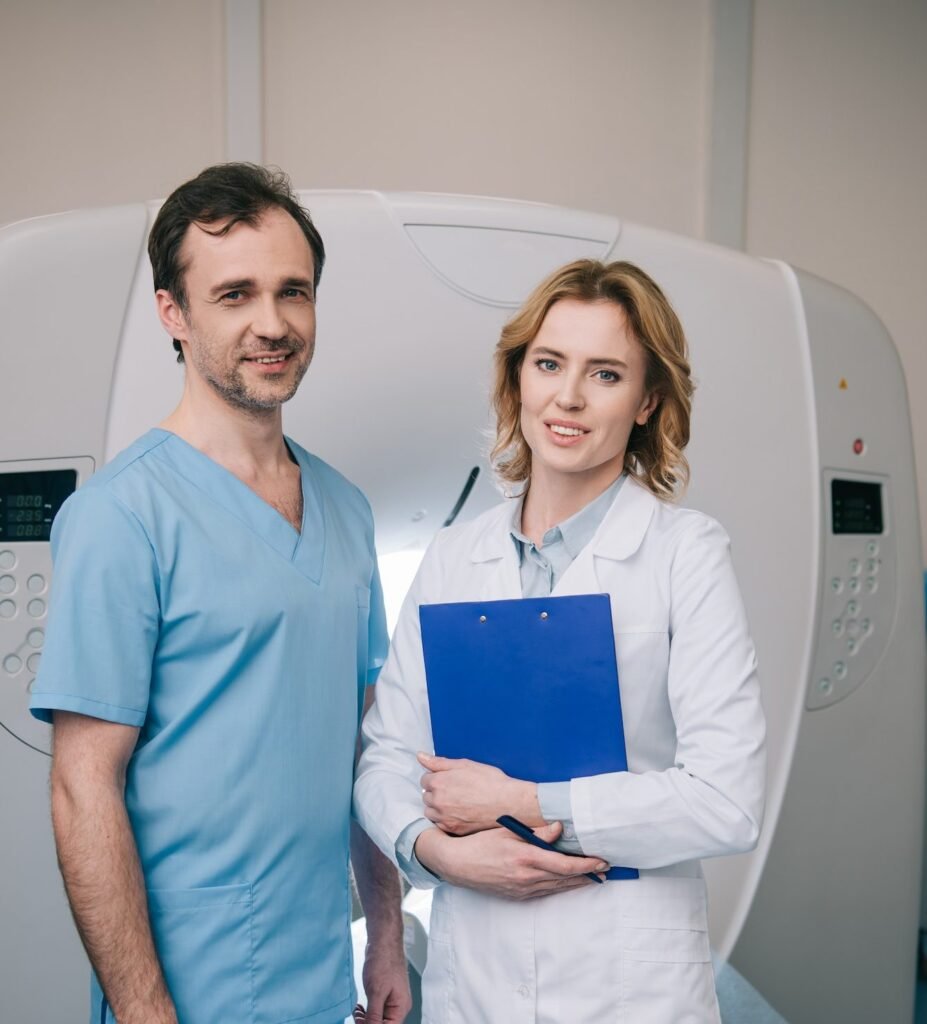 beautiful radiologist holding clipboard while standing near assistant and looking at camera e1682350841592